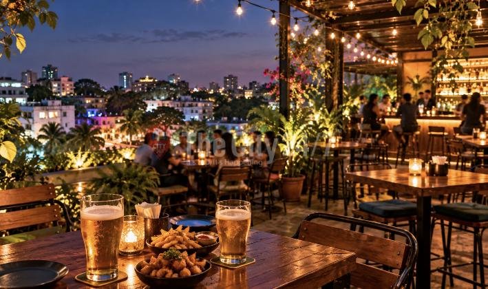 Two pints of beer, fries and a snack bowl on a candlelit table on a rooftop bar terrace with string lights and city views at dusk