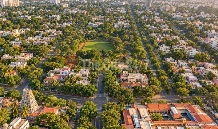 An aerial view of a leafy, grid-planned neighbourhood with a large central park, wide tree-lined roads, low-rise homes and a temple gopuram